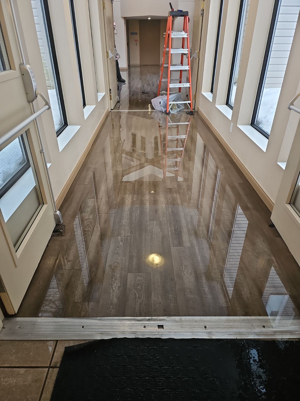 Water damage in strata building common area entryway with ladder and restoration equipment on site